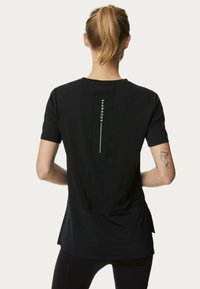 Camiseta atlética negra de manga corta, con tejido texturizado, acentos de malla y la marca blanca "GOODMOVE" en la parte posterior.