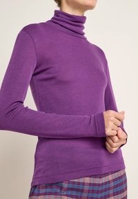 Lila Rollkragenpullover mit weichem, körpernahen Design und langen Ärmeln. Mit hohem Kragen und nahtlosen Bündchen. Kombiniert mit karierter, mehrfarbiger Hose.