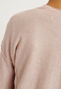 Suéter de punto rosa claro con un tejido texturizado, con un escote amplio y costuras visibles a lo largo de los bordes.