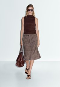 Top marron sans manches à col roulé, culottes en suède marron, sandales plates marron et un grand sac à main marron. Design simple et couleurs neutres.
