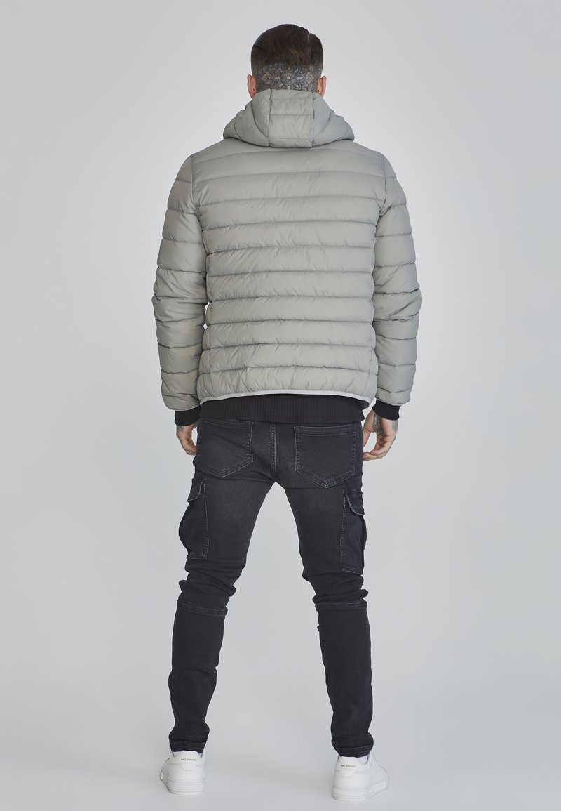 Grau gefütterte Jacke mit Kapuze, horizontale Steppoptik, gerippte Bündchen, kombiniert mit schwarzen Cargo-Hosen und weißen Sneakers.