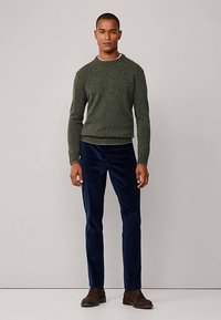 Grüner Strickpullover mit rundem Halsausschnitt und gerippten Bündchen, kombiniert mit marineblauen Cordhosen und braunen Lederstiefeln.