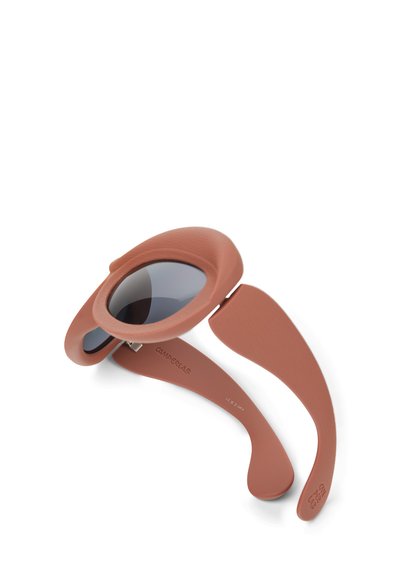 Runda solglasögon i en matt terracotta-båge, med mörkgrå linser och en överdimensionerad design med böjda skalmar.