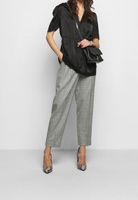 Top de satén negro con mangas abullonadas, combinado con pantalones gris claro ajustados. Acentuado con un bolso acolchado negro y tacones de piel de serpiente.