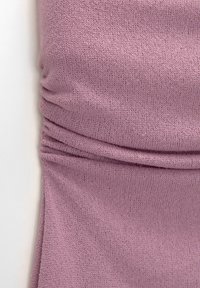 Tissu tricoté rose doux avec des plis froncés et une texture de tricot visible sur un fond pâle.