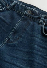 Dunkelblaue Denim-Jeans mit einer glatten Textur, ausgestattet mit einem traditionellen Taillenbund, einem Metallknopf und genähten Taschen.