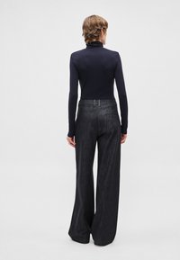 Tumši zils garroku t-krekls ar augstu apkakli, kombinēts ar tumši pelēkām plašām džinsa biksēm. Raksturots ar piegulošu augšdaļu un teksturētu džinsa materiālu ar aizmugurējām kabatām.