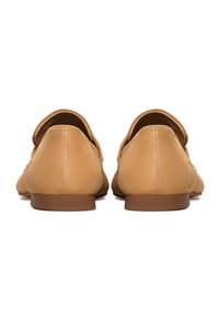 Par af beige ruskind loafers set bagfra med lave brune hæle og synlige syninger langs midtersømmen.