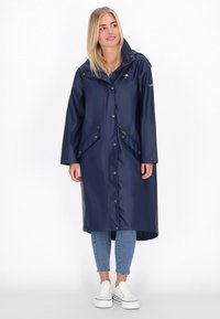 Capa de lluvia impermeable en color navy con capucha, botones a presión y dos bolsillos frontales. Fabricada con material suave, diseño hasta la rodilla y corte casual.