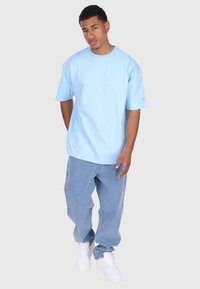 Lyseblå bomulls T-skjorte med korte ermer, kombinert med lyseblå denim jeans og hvite joggesko, står mot en nøytral bakgrunn.