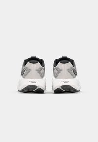 Chaussures de sport noires et grises avec une tige en tissu texturé, une semelle rembourrée et une languette au niveau du talon. Des motifs géométriques discrets sont présents.
