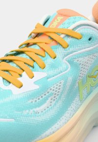 Aqua blue running shoe with orange accents, mesh upper, textured pattern, yellow laces, and white branding logo on the side.