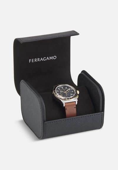 Orologio con cinturino in pelle marrone in una confezione nera. Presenta un quadrante nero, dettagli dorati e una cassa in acciaio inossidabile con una finitura testurizzata.