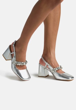 Silver metallic heeled shoes with a block heel, open-back design, and a decorative rhinestone strap across the instep.