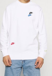Sudadera blanca de algodón con puños acanalados, que presenta logotipos multicolor de Nike en negro, azul y rojo en el frontal y la manga.