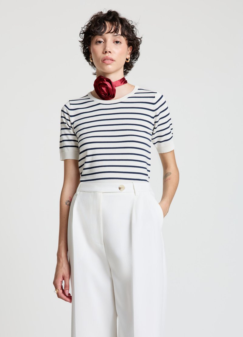 Gestreiftes Strickoberteil in Weiß mit marineblauen Streifen, kurzen Ärmeln und rundem Ausschnitt, kombiniert mit weißen Hosen mit weitem Bein und einem roten Satinschal.