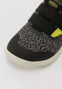 Scarpa nera e grigia con motivo, superiore in maglia testurizzata, punta in gomma, cinturini in Velcro e suola in gomma di colore chiaro.