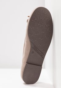 Semelle d'une chaussure en daim beige montrant une semelle extérieure en caoutchouc brun texturée avec la marque "Tamaris", taille 37, et des crampons à motif.