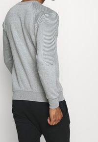 Felpa grigia con dettagli a coste sulla spalla sinistra e sulla manica, caratterizzata da scollo rotondo e polsini a costine. Realizzata in morbido materiale misto cotone.