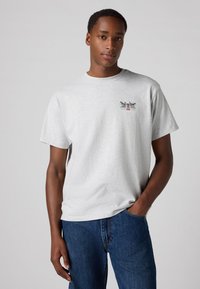 Gray cotton t-shirt with a crew neck, short sleeves, and a graphic print featuring two dogs and text on the chest. Worn with blue jeans.