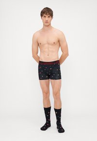 Fekete boxer alsónadrág piros derékkal, sokszínű virágmintákkal. Fekete zoknik hasonló virágmintákkal.