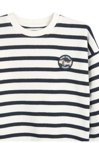 Maglione a righe con collo tondo in bianco e blu navy con una texture morbida. Presenta un patch rotondo con una grafica di un cane e il testo "Marc O'Polo Friends".