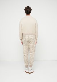 Μπεζ πουλόβερ με ριμπ τελείωμα, συνδυασμένο με μπεζ παντελόνια με στενή γραμμή και μοτίβο στο ίδιο χρώμα. Λευκά αθλητικά παπούτσια με φωτεινές σόλες.