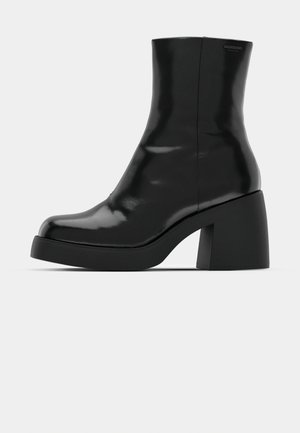 Schwarze Stiefeletten mit glänzender Oberfläche, quadratischer Zehenpartie und dicker Blockabsatz. Das Design zeichnet sich durch eine nahtlose Silhouette und minimalistische Markenkennzeichnung aus.