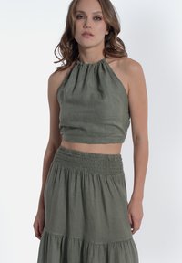 Top halter in lino verde abbinato a una gonna con vita arricciata coordinata, caratterizzata da un design a strati che mette in mostra un aspetto morbido e tessurizzato.