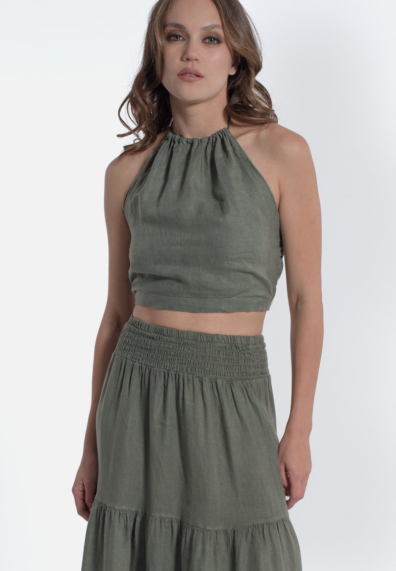Top halter in lino verde abbinato a una gonna con vita arricciata coordinata, caratterizzata da un design a strati che mette in mostra un aspetto morbido e tessurizzato.