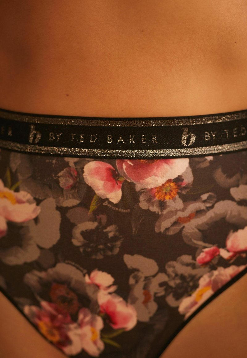 Lille lillekirjaga naiste aluspesu, mille tumedat tausta kaunistavad lilled, pehme kangas ja läikiv must vöö, millel on kiri "By Ted Baker."