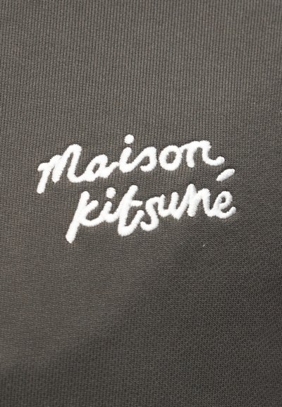 Λευκό κεντημένο κείμενο "Maison kitsuné" σε σκουρόχρωμο γκρι ριμπ ύφασμα.