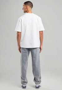 White cotton t-shirt with a relaxed fit and short sleeves, paired with gray corduroy pants, and white sneakers with navy accents.