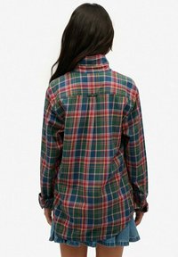 Chemise à carreaux avec un schéma de couleurs vert, rouge et bleu, dotée de manches longues, d'un col et d'un ourlet arrière plus long. En matériau coton.