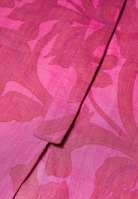Rosa stof med mørkere rosa abstrakte blomster mønstre og et syet rektangulært stofdetalje, der overlapper mønsteret.