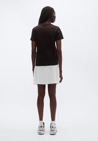 Melnā īsroku T-krekls kopā ar baltu kroku svārku, valkāts ar gaišām sporta kurpēm, skatīts no aizmugures.