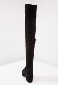 Bottes noires montantes au-dessus du genou en suédine, talons épais et détail zippé sur le côté. Design sans coutures qui met en valeur la silhouette.