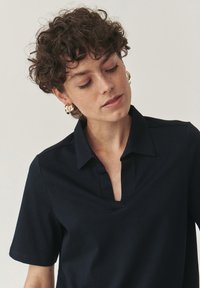Polo shirt blu navy con colletto corto, realizzato in un tessuto liscio. Presenta una patta parziale e maniche corte. Senza motivi visibili o decorazioni.
