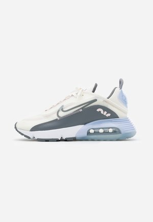 Zapatilla Nike Air Max 2090 blanca y gris con suela de amortiguación de aire azul translúcido y logo swoosh gris sobre fondo liso.