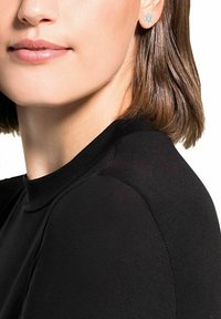 Pendientes de plata con un diseño floral, llevados por una persona con el cabello corto y liso castaño, sobre una blusa negra ajustada.