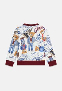 Sweatshirt blanc avec des illustrations d'ours, des tenues en denim bleu et des accents bleu marine. Comprend divers logos graphiques ainsi qu'un col et des poignets côtelés bordeaux.