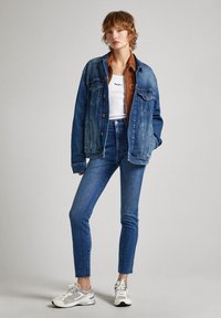 Jeansjacka och högmidjade jeans i varierande blå nyanser, kombinerade med en vit tanktop. Sneakrar med grå och vita accenter.