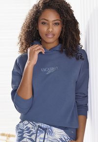 Felpa con cappuccio blu navy con stampa "VACATION" in grigio chiaro e polsini a costine. Abbinata a pantaloni corti azzurri chiari con un design floreale.