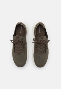 Green mesh sneakers with brown laces, featuring a textured surface and a white rubber outsole. Brand logo visible on the insole.