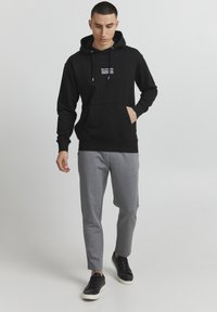 Sort hættetrøje med snore og frontlomme, parret med lysegrå tapered sweatpants og sorte sneakers. Enkel, afslappet design.