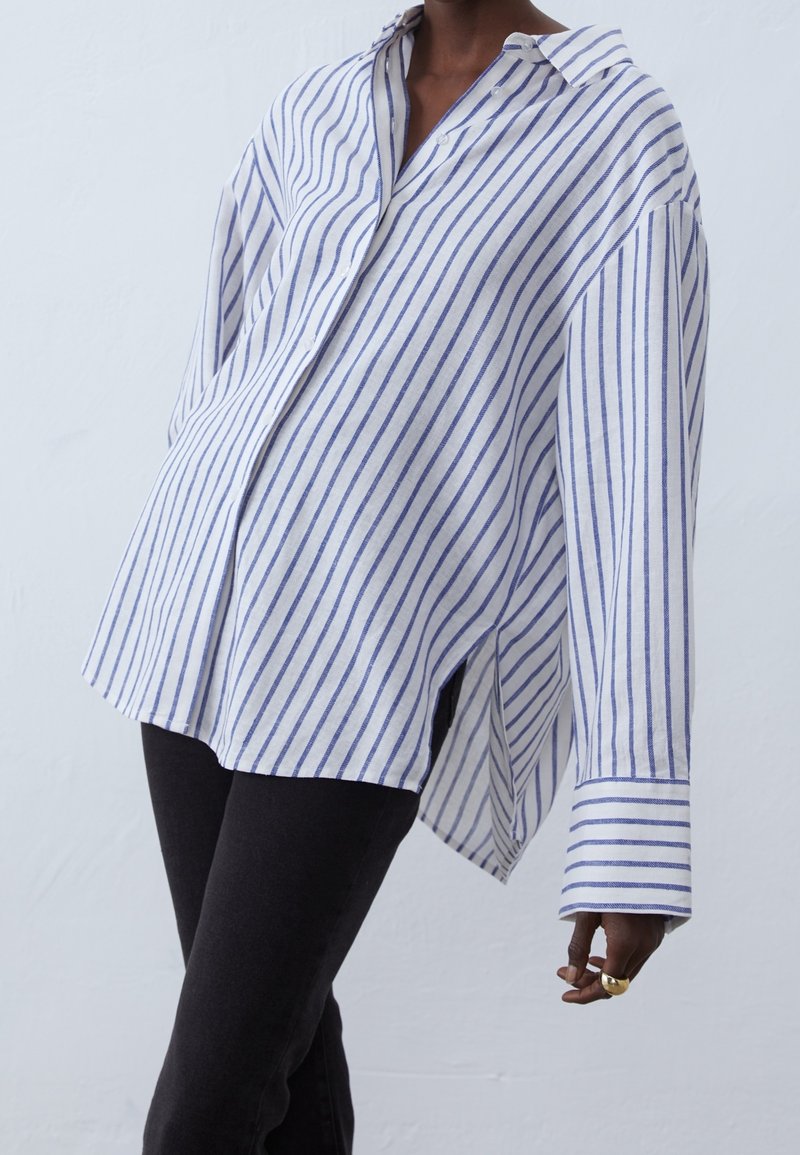 Striped shirt in white and blue, made of lightweight fabric, features a relaxed fit, button-down collar, and side slits for movement.