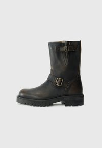 Botas de cuero negro hasta la mitad de la pantorrilla con dos correas decorativas y hebillas, suela resistente y ligeros detalles de desgaste.
