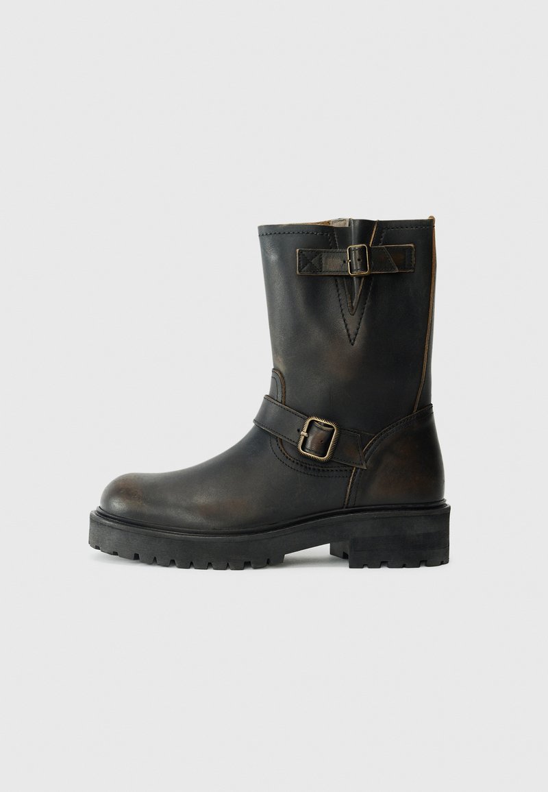 Botas de cuero negro hasta la mitad de la pantorrilla con dos correas decorativas y hebillas, suela resistente y ligeros detalles de desgaste.