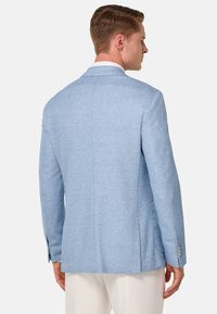 Blazer azul claro con tejido texturizado, solapas con muescas y dos aberturas traseras. Presenta botones en las mangas y bolsillos laterales.