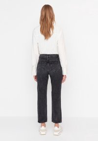 Jean en denim noir avec une coupe décontractée, taille haute et poches arrière, associé à une chemise blanche à manches longues rayée et des baskets blanches.